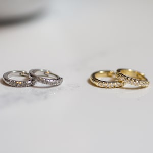 Puede incluir: Dos pares de pendientes de aro, un par es de plata con piedras transparentes y el otro par es de oro con piedras transparentes.