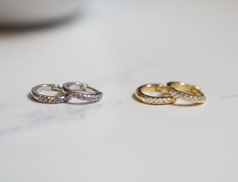 Puede incluir: Dos pares de pendientes de aro, un par es de plata con piedras transparentes y el otro par es de oro con piedras transparentes.