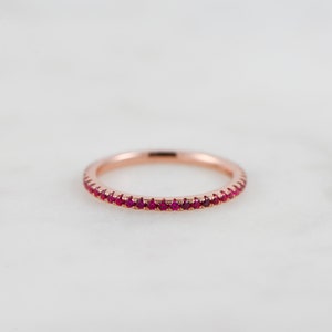 May include: A delicate rose gold band ring with a row of small, bright red ruby stones.