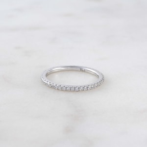 May include: A silver band ring with a row of small clear stones around the entire band. The ring is marked "925" on the inside.