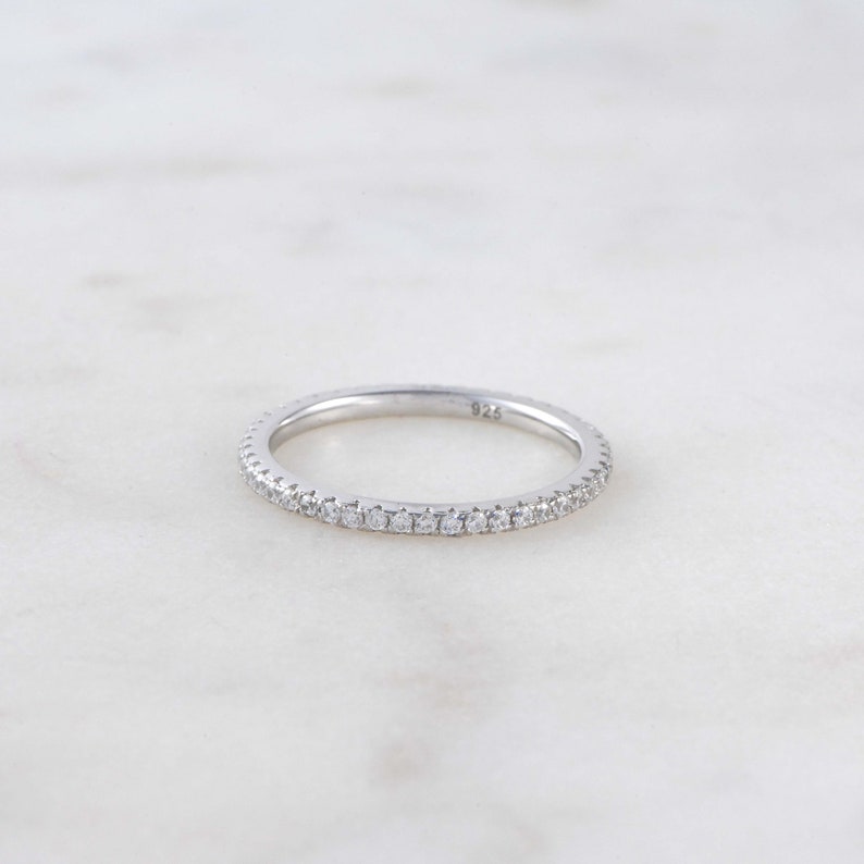 May include: A silver band ring with a row of small clear stones around the entire band. The ring is marked "925" on the inside.