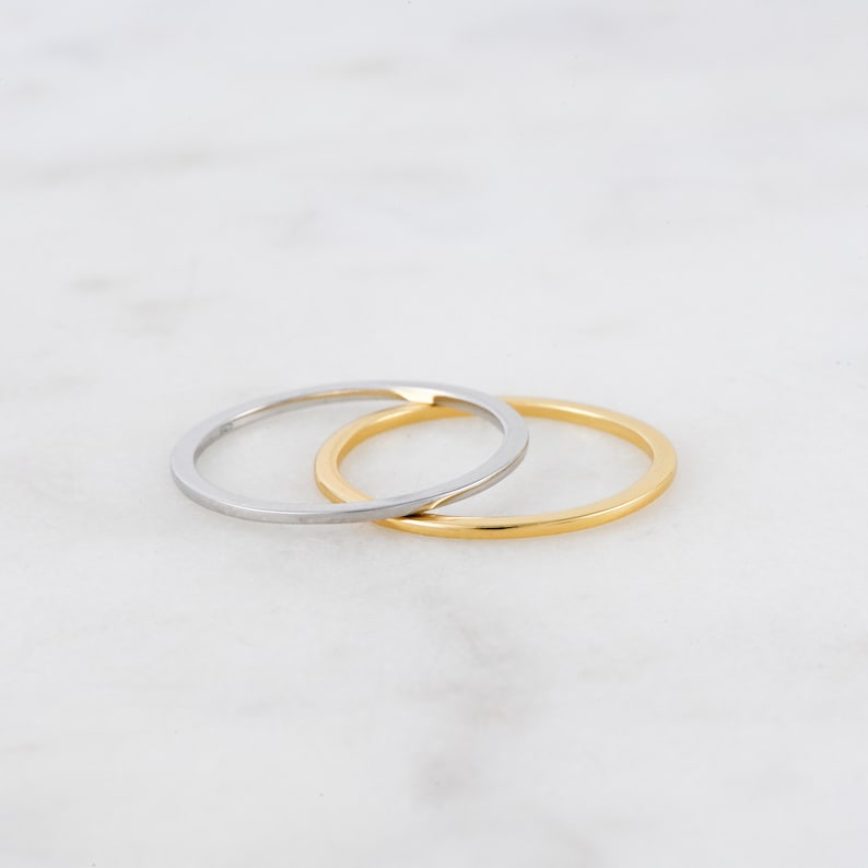 May include: Two thin rings, one gold and one silver, are stacked on top of each other. The rings are simple and elegant.