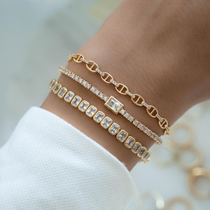 model wearing a chain cz gold bracelet, a tennis bracelet with a bezel emerald cut charm and a bezeled emerald cut tennis bracelet