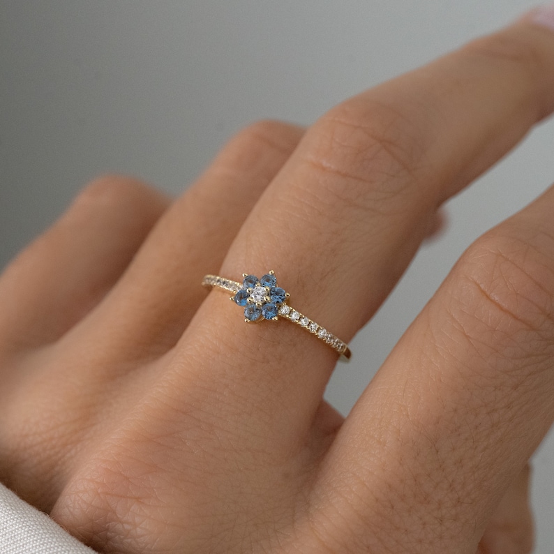 May include: A delicate gold ring with a flower-shaped design featuring blue and white gemstones.