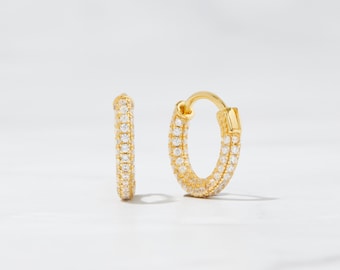 May include: A pair of gold hoop earrings with a row of clear cubic zirconia stones around the hoop.