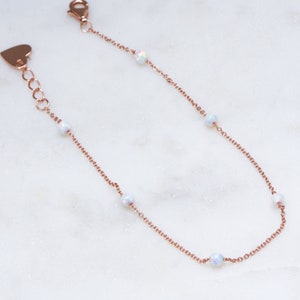 May include: A delicate rose gold chain bracelet with five opal beads. The bracelet has a heart-shaped clasp.