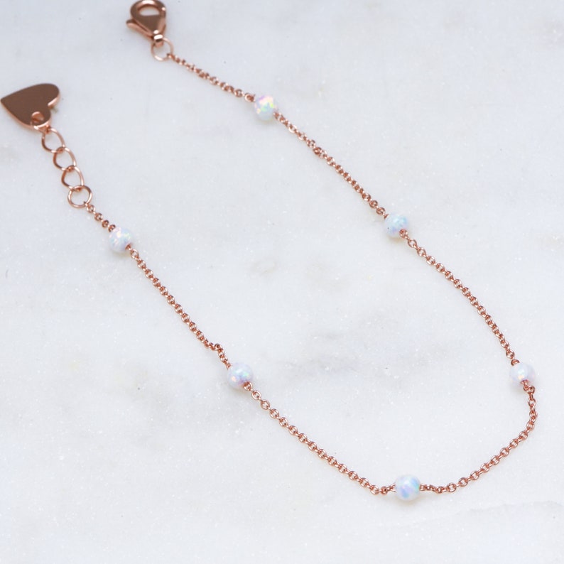 May include: A delicate rose gold chain bracelet with five opal beads. The bracelet has a heart-shaped clasp.