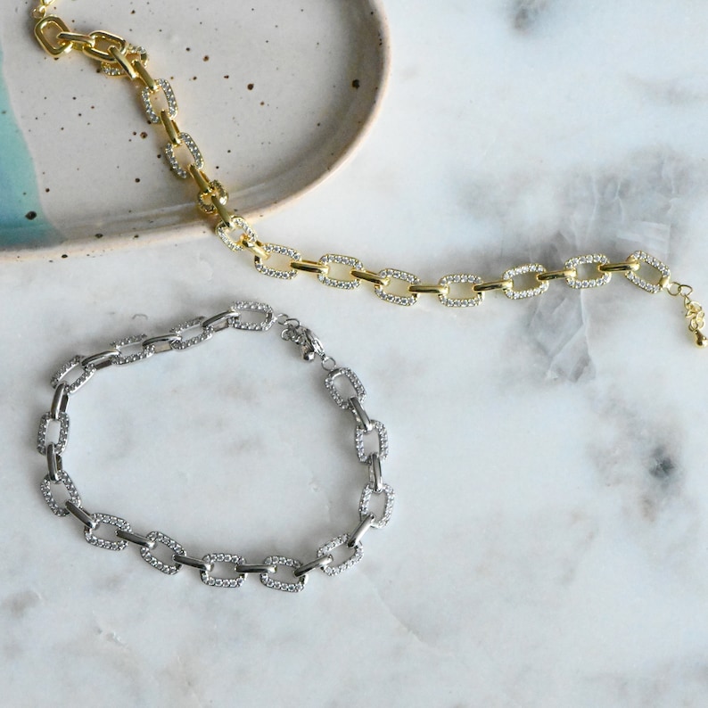 May include: Two chain necklaces with square links, one gold and one silver, both with clear rhinestones.