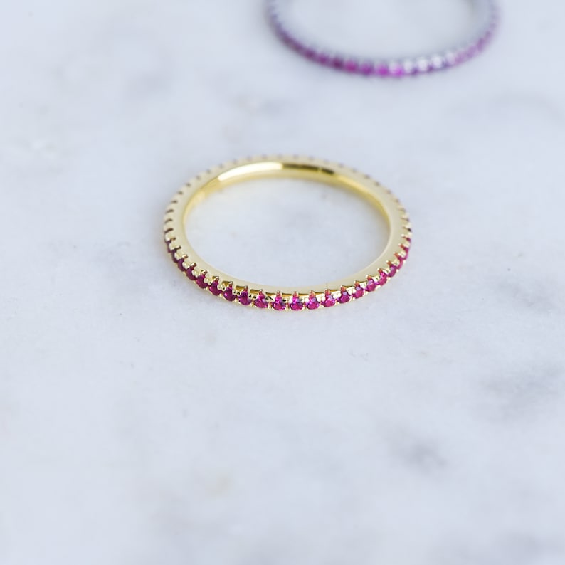Puede incluir: Un anillo de banda de oro con una fila de peque&ntilde;as piedras preciosas rojas alrededor del borde.