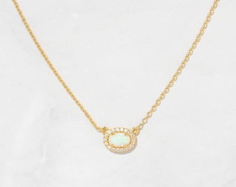 May include: A delicate gold chain necklace with a small oval pendant featuring a white opal surrounded by a halo of tiny clear cubic zirconia stones.