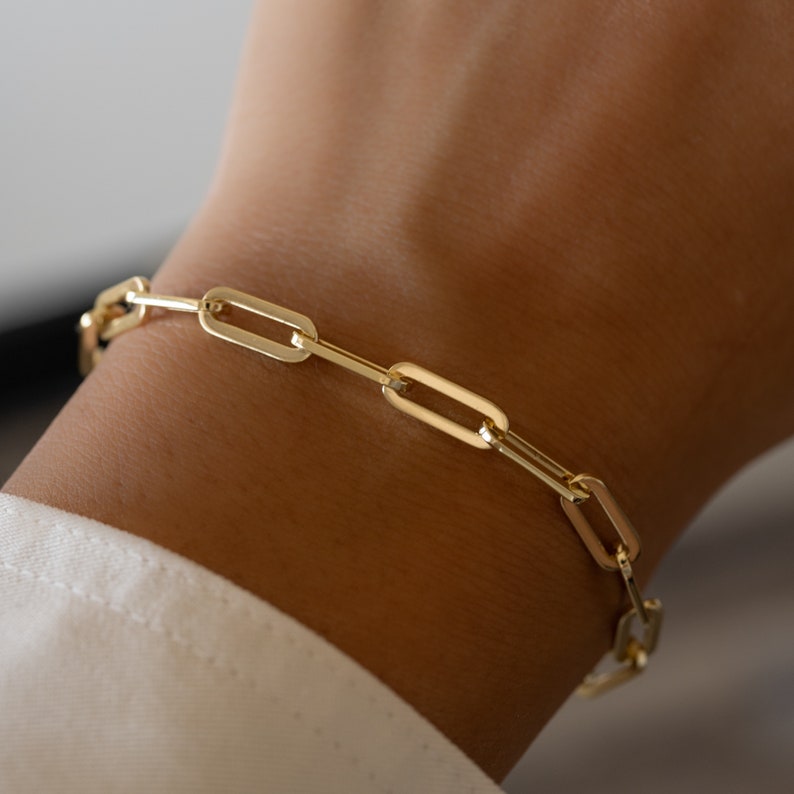 May include: A gold chain bracelet with a linked design. The bracelet is made of oval-shaped links.