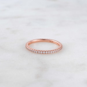 May include: A rose gold band ring with a row of small clear stones around the entire band. The ring is marked "925" on the inside.