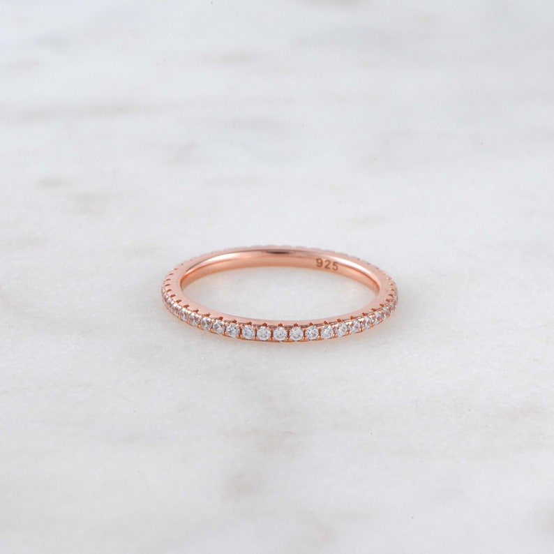 May include: A rose gold band ring with a row of small clear stones around the entire band. The ring is marked "925" on the inside.