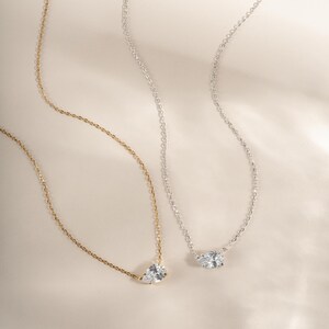 Gold chain layering necklace and a silver gemstone necklace on a plain background
