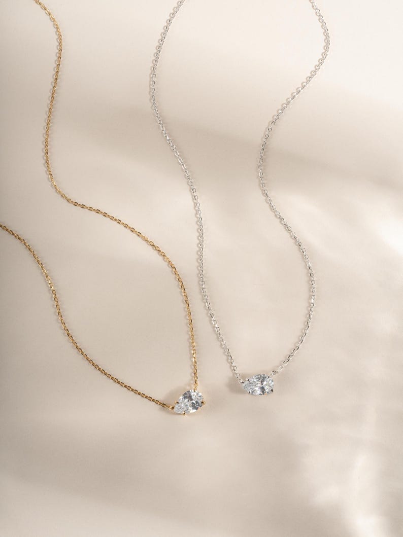 Gold chain layering necklace and a silver gemstone necklace on a plain background