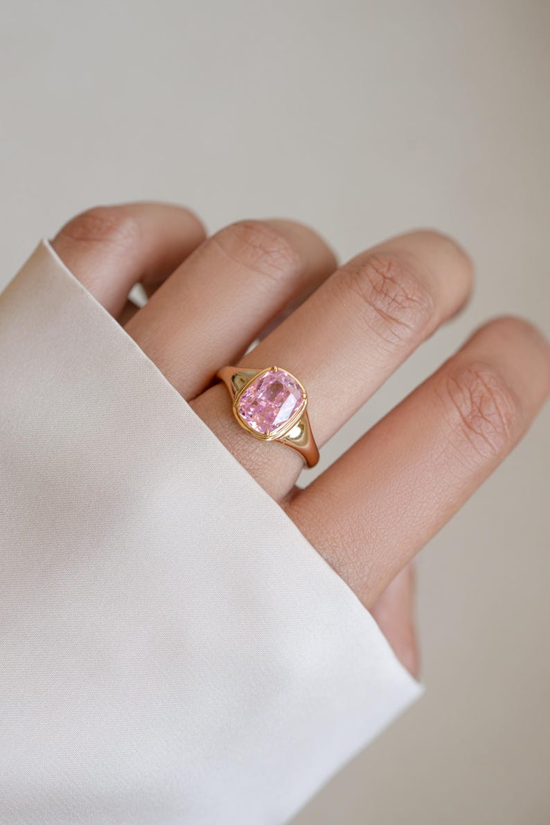 Elongated pink cubic zirconia ring in gold, worn on the hand as a cushion cut statement ring
