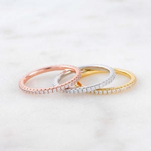 May include: Three thin diamond eternity bands in rose gold, white gold, and yellow gold.