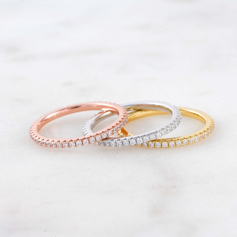 May include: Three thin diamond eternity bands in rose gold, white gold, and yellow gold.
