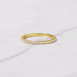May include: A thin gold band with a row of small diamonds set around the entire band.