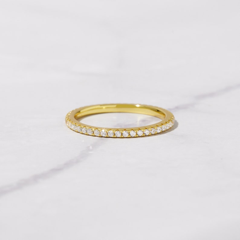 May include: A thin gold band with a row of small diamonds set around the entire band.