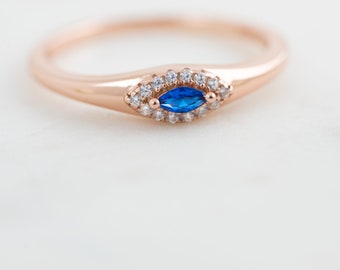 May include: A rose gold ring with a blue marquise-shaped gemstone surrounded by a halo of smaller clear gemstones.