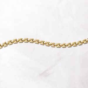 Pode incluir: Um bracelete de corrente de ouro com um design de corrente de caixa. A corrente &eacute; feita de pequenos elos quadrados que s&atilde;o conectados uns aos outros.