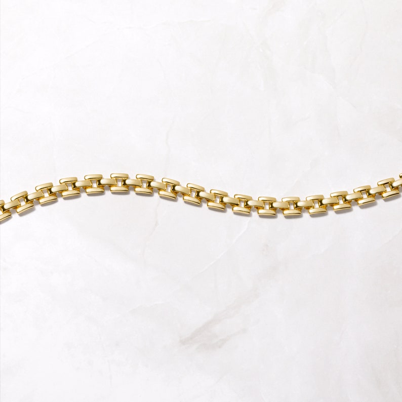 Pode incluir: Um bracelete de corrente de ouro com um design de corrente de caixa. A corrente &eacute; feita de pequenos elos quadrados que s&atilde;o conectados uns aos outros.