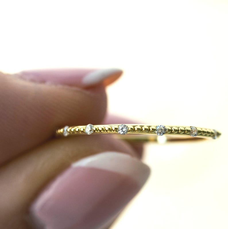 Model holding dainty gold ring with diamonds