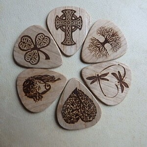May include: Set of seven wooden guitar picks with various laser-engraved designs, including a Celtic cross, a tree of life, a shamrock, a dragonfly, a heart-shaped tree, and a portrait of Jesus.