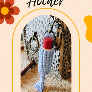 K&ouml;nnte beinhalten: Ein hellblau geh&auml;kelter Lippenpflegestifthalter mit einem roten Lippenpflegestift im Inneren, befestigt an einer Handtasche. Das Bild hat die W&ouml;rter "Chapstick Holder" und "Pattern" in einer dekorativen Schriftart. Der Hintergrund ist beige mit floralen und Regenbogen-Akzenten.