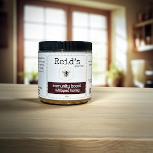 May include: A jar of Reid's gourmet immunity boost whipped honey. The label features a bee graphic and the text "Immunity Boost Whipped Honey". The jar is clear with a black lid and contains a light amber-colored honey. The jar is 8 oz.