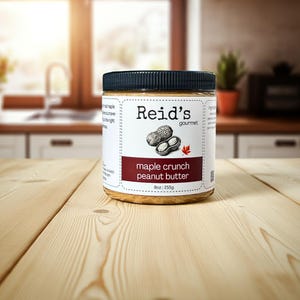 May include: A jar of Reid's gourmet maple crunch peanut butter sits on a wooden surface. The label features a peanut illustration and the text "maple crunch peanut butter." The jar contains 255g of peanut butter and has a black lid.