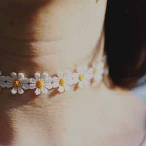 May include: A white choker necklace with yellow daisy flower embroidery.