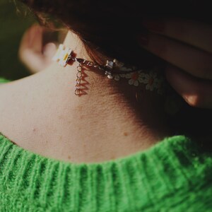 May include: A close-up of a person wearing a green jumper with a white daisy flower choker necklace.