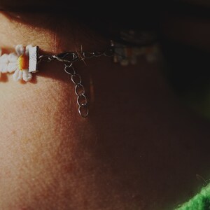 May include: A white daisy flower choker necklace with a silver clasp and chain. The necklace is worn on a person's neck.