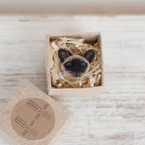 A cute miniature Siamese cat pin in the gift box. The gift box is made of brown craft cardboard.