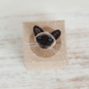 A cute miniature Siamese cat pin on the gift box. The gift box is made of brown craft cardboard.