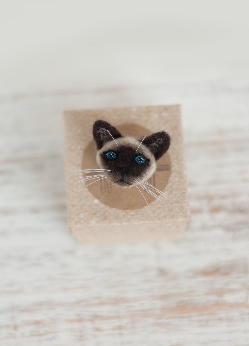 A cute miniature Siamese cat pin on the gift box. The gift box is made of brown craft cardboard.