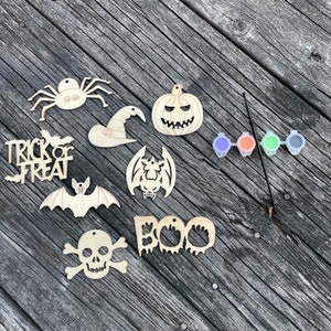May include: A set of nine unfinished wooden Halloween ornaments, including a spider, pumpkin, witch hat, bat, skull and crossbones, "Trick or Treat" sign, and "BOO" sign. The set also includes four small paint pots and a paintbrush.