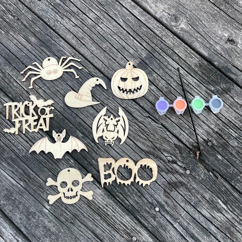 May include: A set of nine unfinished wooden Halloween ornaments, including a spider, pumpkin, witch hat, bat, skull and crossbones, "Trick or Treat" sign, and "BOO" sign. The set also includes four small paint pots and a paintbrush.