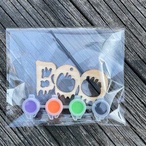 May include: A wooden "BOO" sign with a paintbrush and four small paint pots in purple, orange, green, and black.