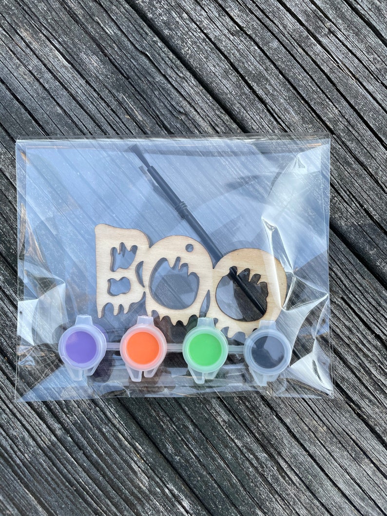 May include: A wooden "BOO" sign with a paintbrush and four small paint pots in purple, orange, green, and black.
