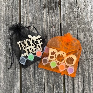 May include: Two Halloween-themed paint-your-own wooden signs in orange and black mesh bags. One sign says "Trick or Treat" and the other says "Boo". Both signs come with six small paint pots.