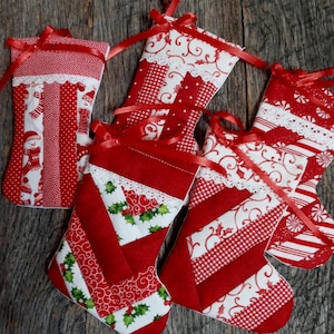 May include: Five red and white Christmas stockings with different patterns. The stockings are made of fabric and have a white lace trim. They are hanging on a wooden surface.