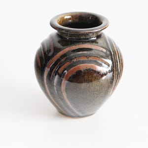 Può includere: Un piccolo vaso rotondo in ceramica con un motivo a spirale marrone scuro e marrone rossiccio. Il vaso ha una finitura lucida e una piccola apertura nella parte superiore. Ceramica fatta a mano, adatta per l'arredamento della casa.