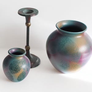 Peut inclure: Deux vases en céramique décoratifs et un bougeoir. Les vases sont ronds avec un dégradé de couleurs teal, violet et or. Le bougeoir est sombre avec un accent en laiton.