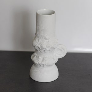 Puede incluir: Jarrón de cerámica blanca con una superficie texturizada que se asemeja a la corteza de un árbol y un asa en forma de concha.