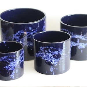 Op de afbeelding: Vier cilindrische keramische plantenbakken in verschillende maten. De plantenbakken zijn diep marineblauw met een textuur, wit en blauw spetterontwerp. Geschikt voor binnen of buiten.