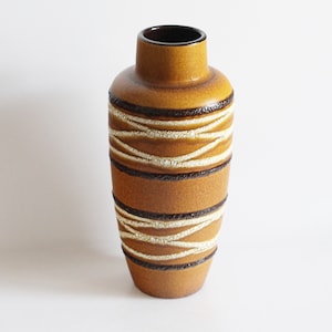 Könnte beinhalten: Eine hohe, braune Keramikvase mit einem weißen und braunen geometrischen Muster. Die Vase hat einen abgerundeten Boden und eine schmale Öffnung.
