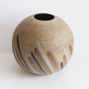 May include: A round ceramic vase with a brown, white, and black geometric pattern. The vase has a wide opening at the top.